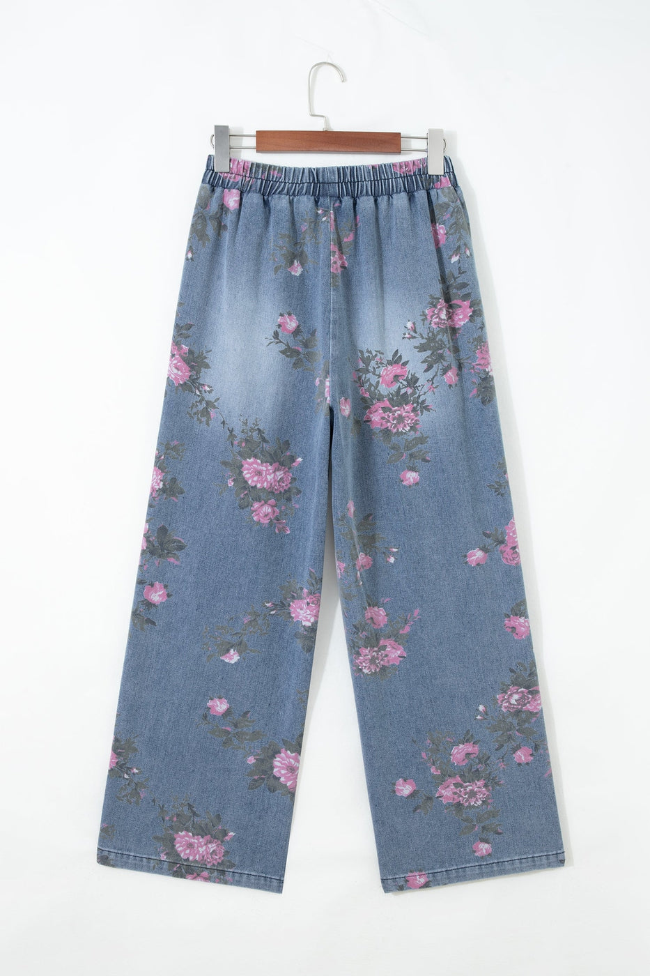 Floral Pull-On Jeans with a wide-leg, light blue denim design and elastic waistband, featuring an all-over pink and purple floral print, hanging on a hanger against a white background.
