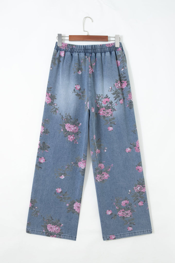 Floral Pull-On Jeans with a wide-leg, light blue denim design and elastic waistband, featuring an all-over pink and purple floral print, hanging on a hanger against a white background.