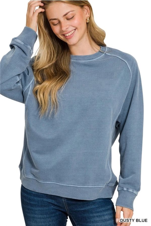 A person wearing a dusty blue, enzyme-washed Pigment Dye French Terry Sweatshirt with ribbed trim and a relaxed fit.