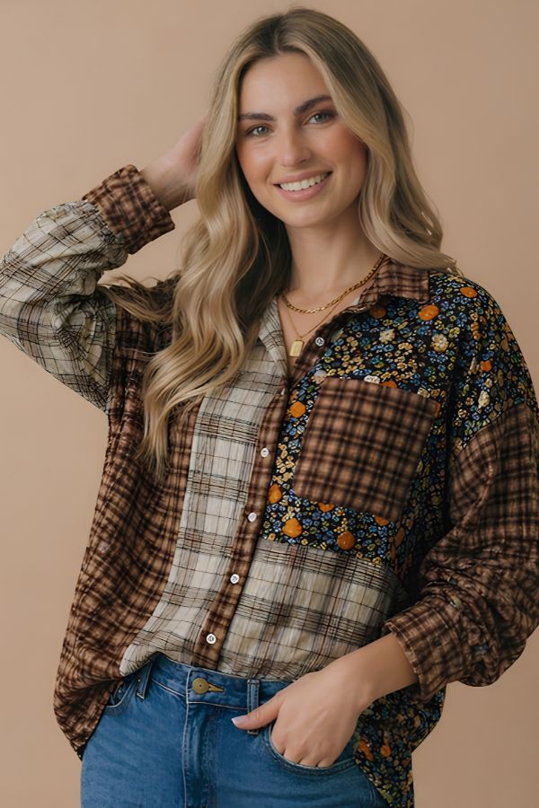 A smiling woman with long, wavy blonde hair wears the Patchwork Button Down Top—a relaxed fit shirt featuring plaid and floral patterns—paired with blue jeans and gold necklaces, standing against a beige background.