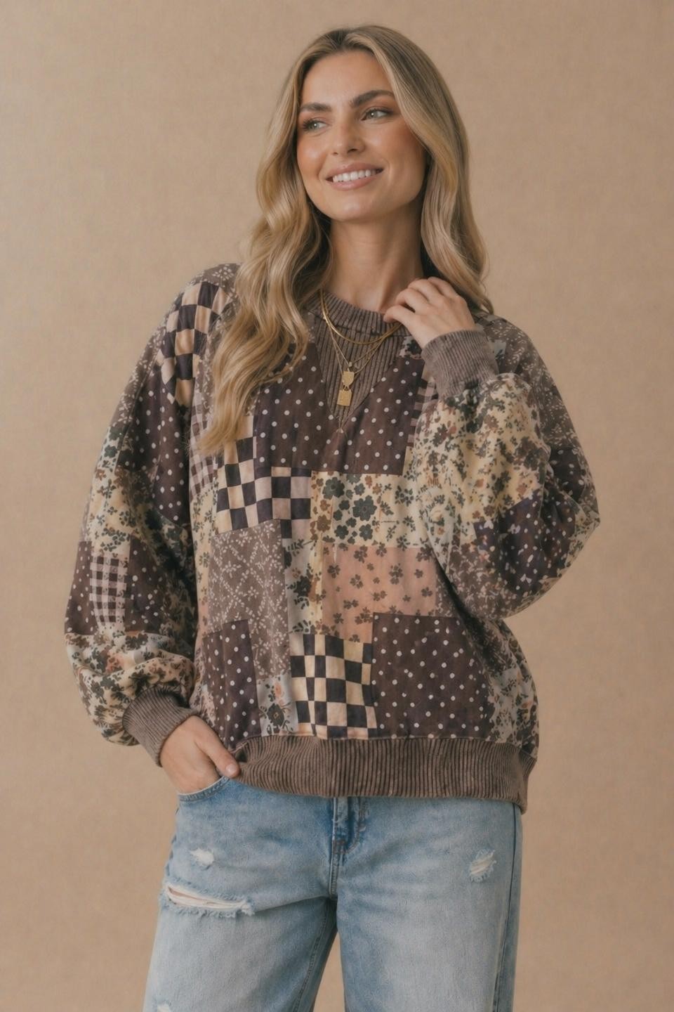 Smiling woman with long blonde hair wearing the Patchwork Oversized Pullover and light blue ripped jeans, standing against a plain beige background.