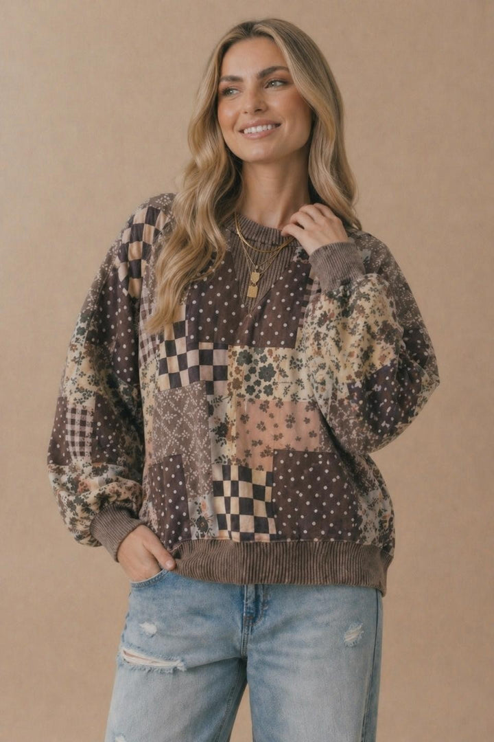 Smiling woman with long blonde hair wearing the Patchwork Oversized Pullover and light blue ripped jeans, standing against a plain beige background.