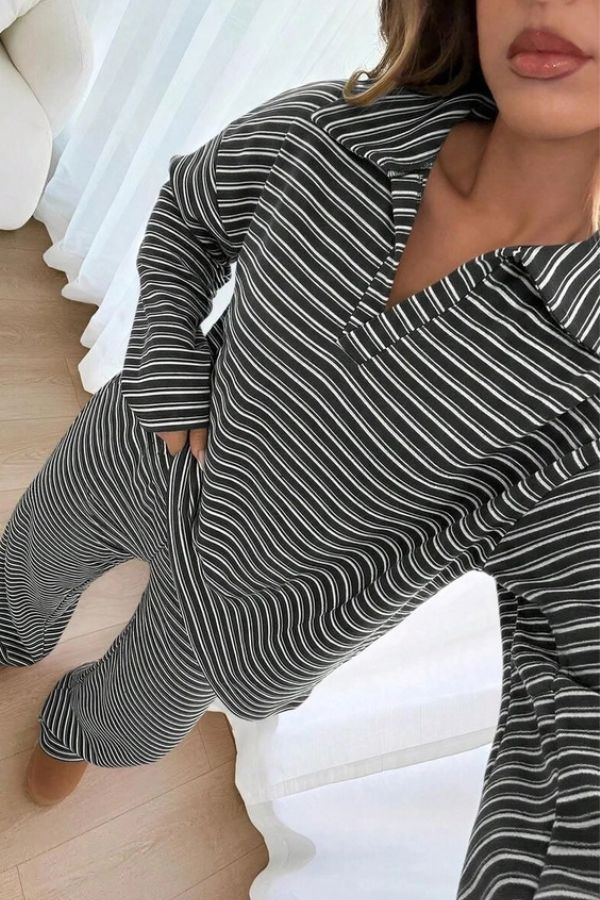 A person wearing the Striped Collared Lounge Set, which features a matching black and white striped pullover with a collar and wide-leg pants, stands indoors on a light wooden floor near white curtains.