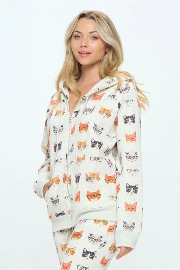 A person wearing an oversized Cats in Glasses Zip Hoodie featuring an all-over pattern of illustrated cats wearing glasses.