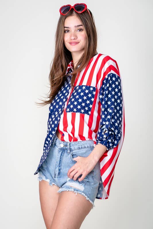 A woman in a Patriotic Button Shirt, heart-shaped red sunglasses, and distressed denim shorts stands against a plain white background, smiling slightly.