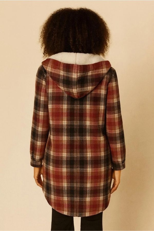 A person with curly hair is shown from the back, wearing the Fur Lined Plaid Hooded Shacket in red, black, and white paired with black pants against a beige background. The cozy shacket’s fur lining adds warmth and style to the look.
