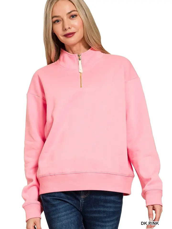 A woman with long blonde hair is wearing a relaxed fit, light pink Fleece Half Zip Sweatshirt crafted from soft fabric and blue jeans, posing and smiling at the camera against a white background.