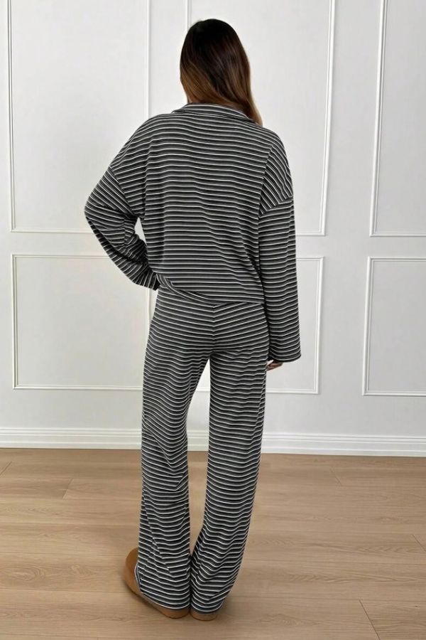 A person stands indoors with their back to the camera, wearing the Striped Collared Lounge Set—a chic black and white striped two-piece featuring a collared pullover top and wide-leg pants. The setting includes white paneled walls and light wood flooring.
