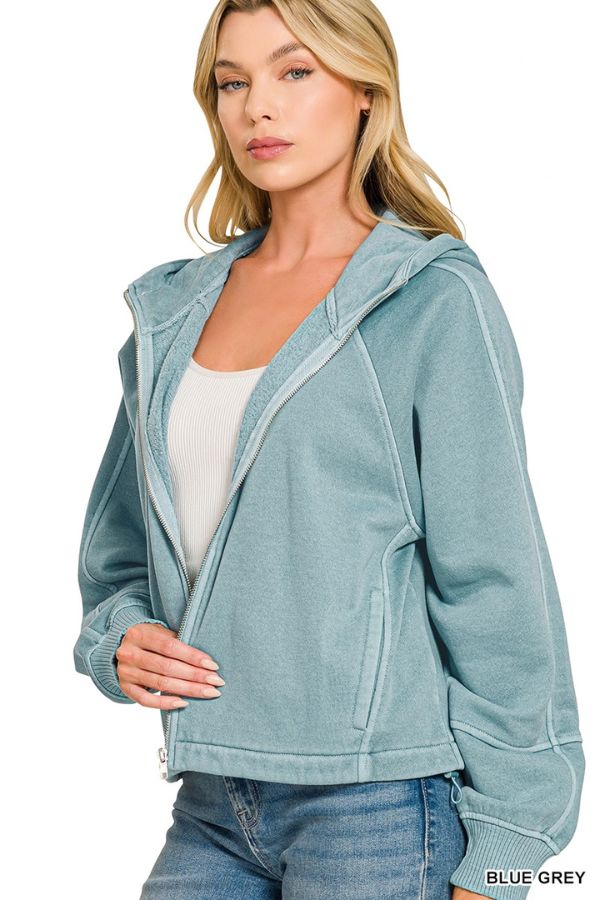 Woman in a Pigment Dye Zip Up Hoodie (light blue-gray) with adjustable hem, over a white top and blue jeans, standing against a white background. She has long blonde hair and a neutral expression.