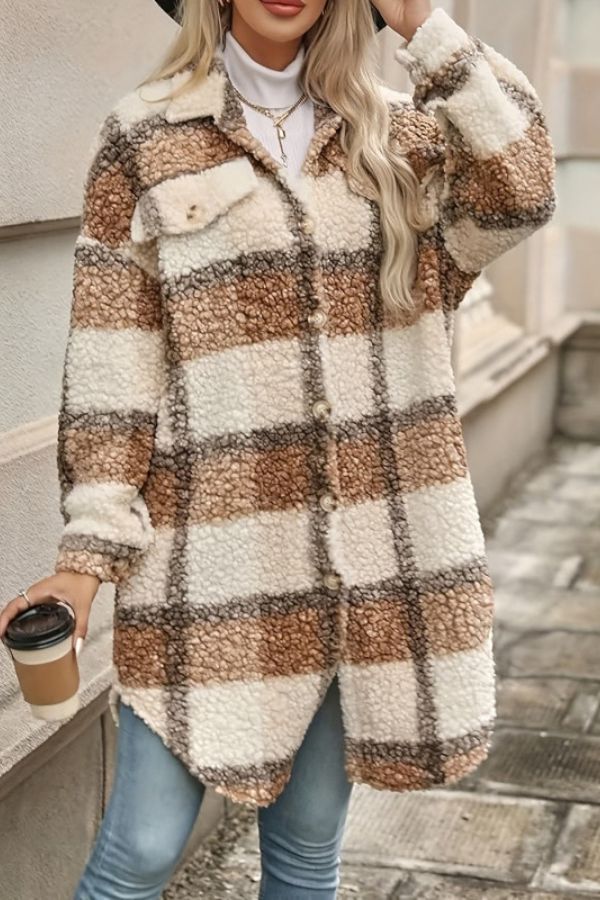 A person wearing a longline, button-front, plaid teddy fleece coat and blue jeans, holding a disposable coffee cup.