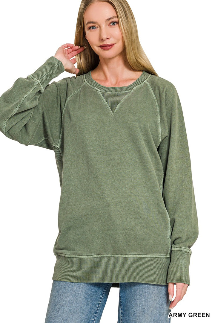 A woman stands with one hand touching her hair, wearing the Pigment Dyed Pullover in army green—an oversized, relaxed-fit French terry sweatshirt featuring ribbed cuffs and hem—effortlessly paired with light blue jeans.