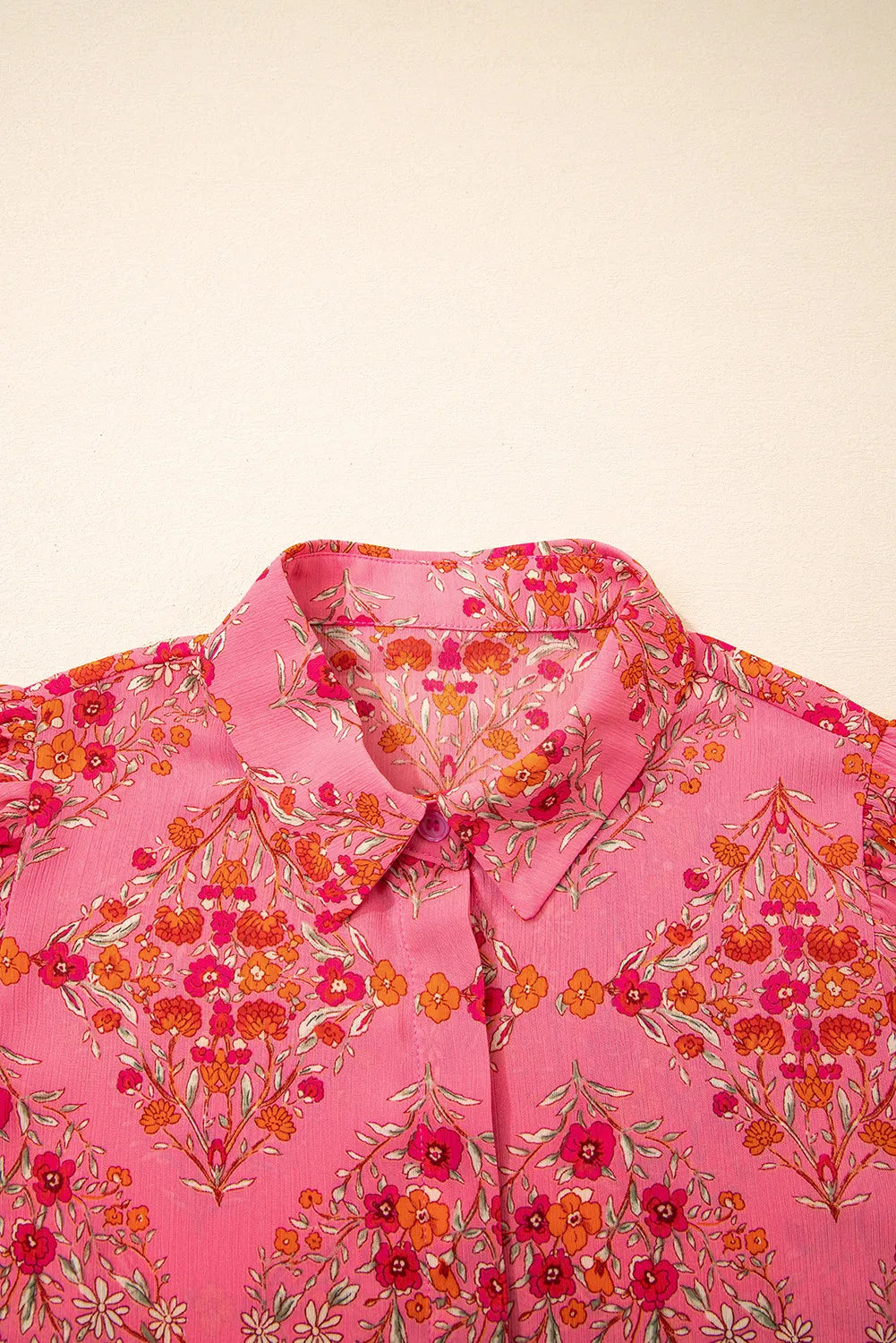 A close-up of the Floral Puff Sleeve Blouse, crafted from pink fabric with a vibrant red, orange, and white floral pattern. This lightweight women's top is shown against a plain light background, perfect for any occasion.