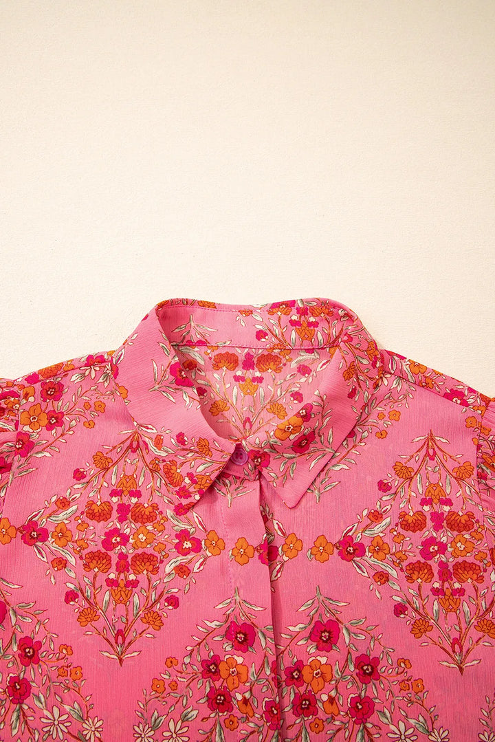 A close-up of the Floral Puff Sleeve Blouse, crafted from pink fabric with a vibrant red, orange, and white floral pattern. This lightweight women's top is shown against a plain light background, perfect for any occasion.