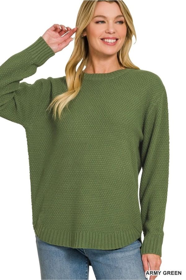 A woman wearing the Everyday Crew Neck Sweater in army green, featuring a textured knit and long sleeves, paired with light blue jeans. She is smiling and touching her hair. This relaxed fit sweater is perfect for everyday wear. The background is plain white.