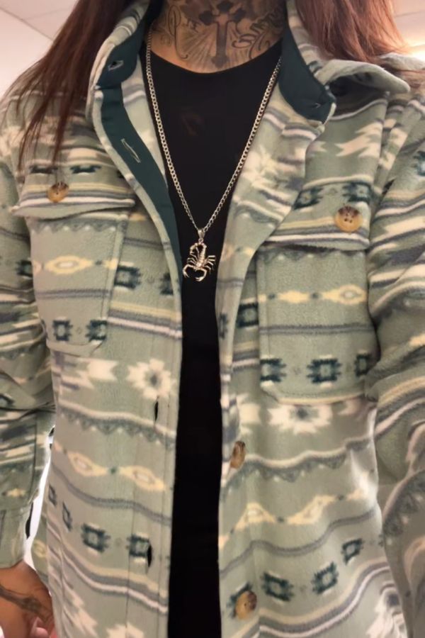 A person wearing the Southwestern Fleece Shacket over a black shirt, accessorized with a silver scorpion pendant necklace, with visible neck tattoos.