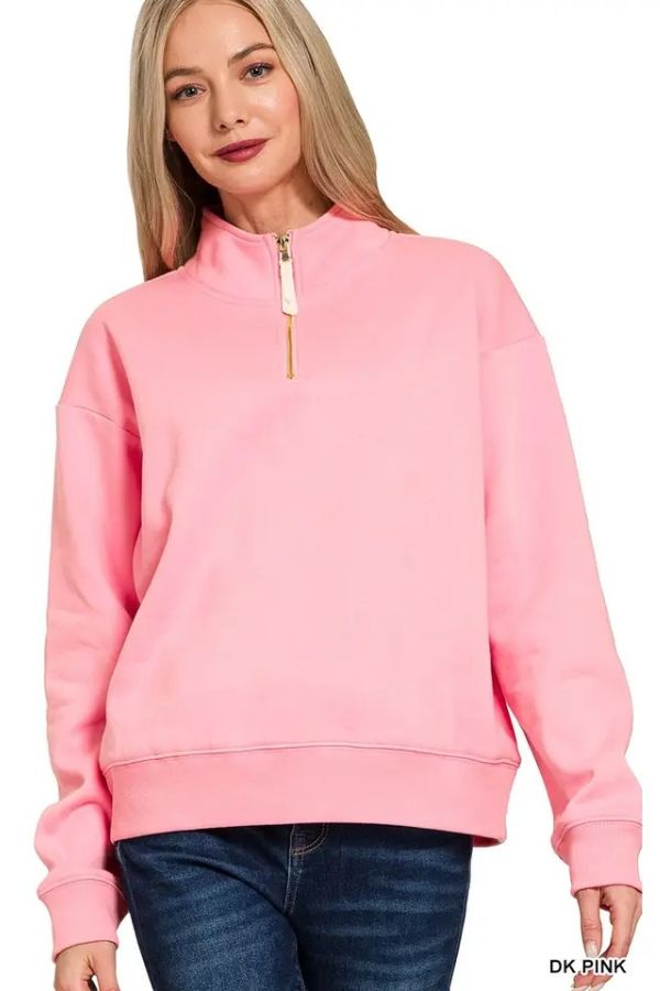 A woman with long blonde hair is wearing a relaxed fit, light pink Fleece Half Zip Sweatshirt crafted from soft fabric and blue jeans, posing and smiling at the camera against a white background.