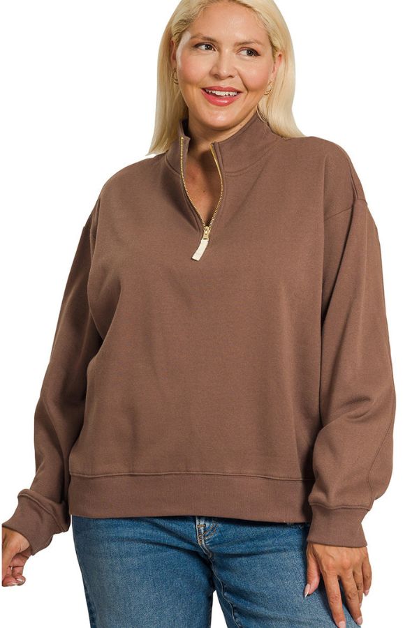 A woman wearing a brown long-sleeve quarter-zip sweatshirt and blue jeans, shown from the head down against a plain white background.