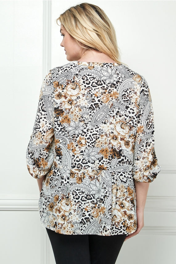 A woman with blonde hair models the Plus Abstract Print Blouse in black, white, and tan with paisley floral and animal patterns. She is facing away from the camera against a light-colored wall.