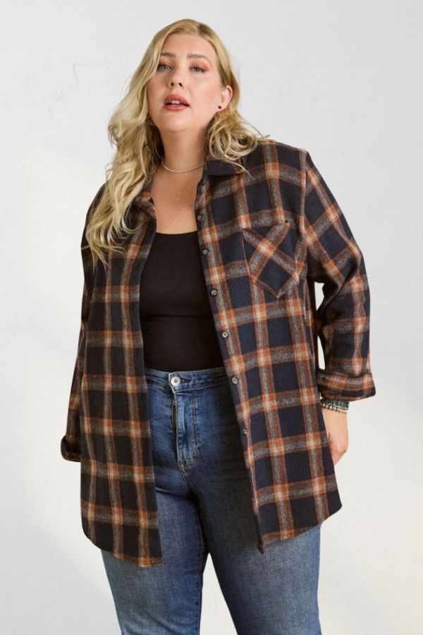 A person wearing a Curvy Plaid Flannel Shirt in an oversized, navy and orange plaid pattern over a black tank top and blue jeans.