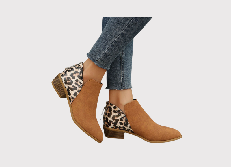 A person wearing brown ankle boots with leopard print accents and blue jeans.