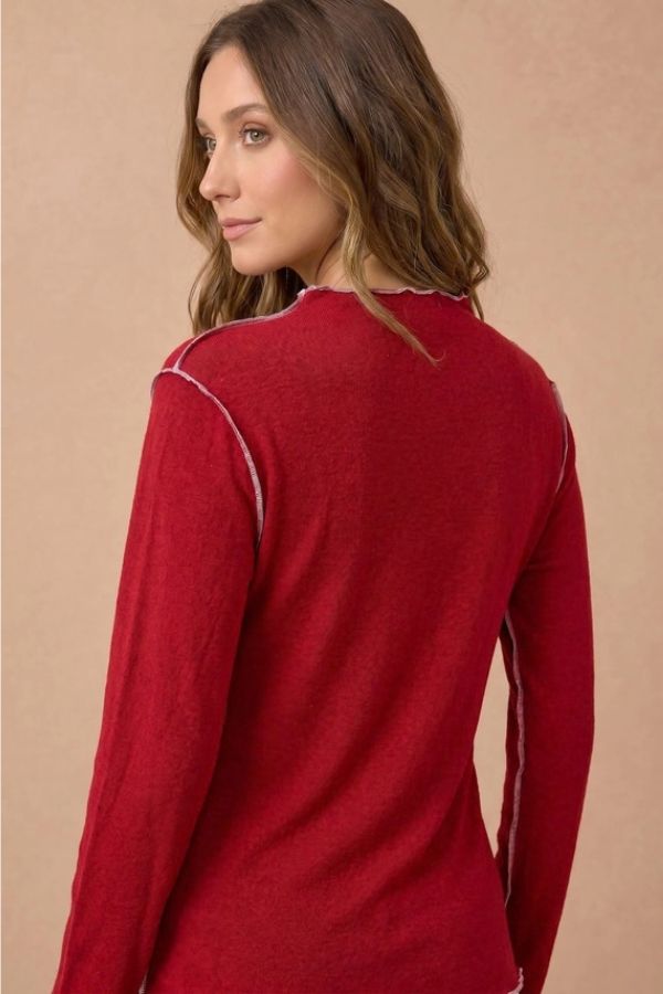 A person wearing a red Frilled Mock Neck Hacci top with long sleeves and visible white contrast stitching along the seams and neckline.