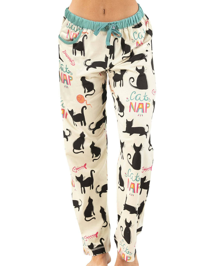 A person wears the Dog Mom, Cat Nap & More Pajama Pants—cream pajama pants with black cat silhouettes, yarn balls, colorful "Cat NAP" text, and a comfy teal drawstring waistband.