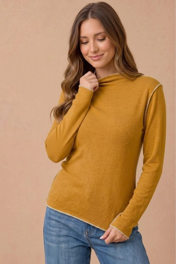 A woman wearing a mustard yellow Frilled Mock Neck Hacci Top with exposed light-colored seam detailing.