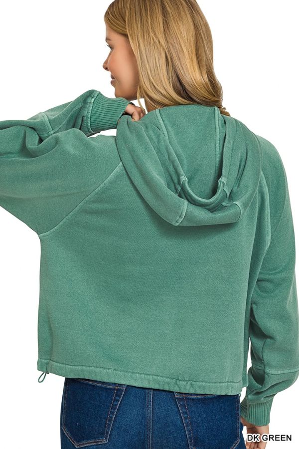 A woman with long blonde hair wears a relaxed fit Pigment Dye Zip Up Hoodie in green and blue jeans, facing away from the camera with her head turned to the side.