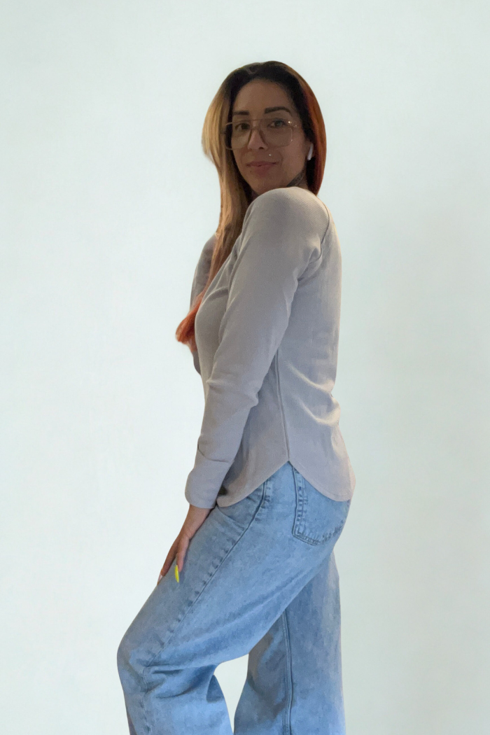 A woman with long, straight hair and glasses poses confidently against a plain light background, wearing a Waffle Knit Long Sleeve Top and loose blue jeans.
