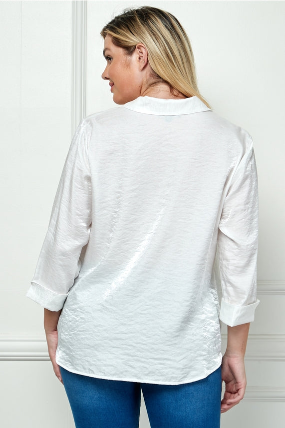 A woman with blonde hair, facing away from the camera, wears the Plus Shimmer Collar Blouse—an oversized white top—paired with blue jeans. She stands against a light-colored paneled wall.