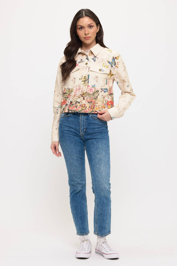 A person with long dark hair and a neutral expression stands against a white background, wearing the Butterfly Floral Jacket over a light shirt, blue jeans, and white sneakers, with one hand in their pocket.