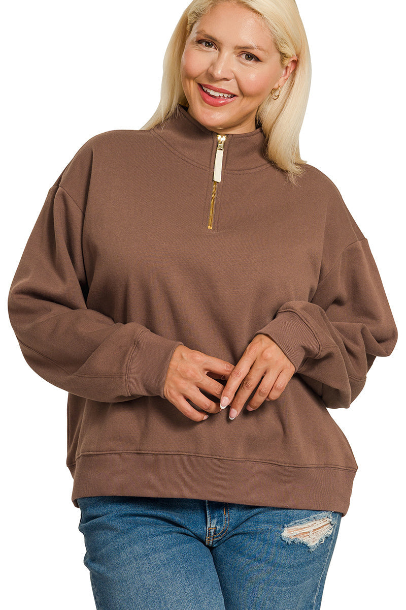 A smiling woman with blonde hair wears the Plus Half Zip Sweatshirt in a relaxed fit and pairs it with blue ripped jeans, standing with her hands loosely clasped in front.