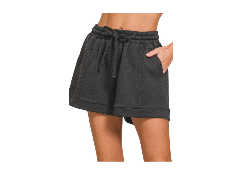 A pair of Zenana Textured Knit Jacquard Drawstring Shorts. These shorts are made of a textured knit fabric with a jacquard pattern, and they have a drawstring waist. The shorts are black and are shown on a model. They are a casual and comfortable style of short, suitable for warmer weather. 