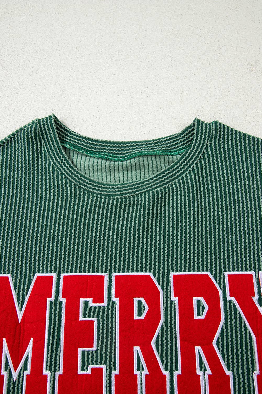 The Merry Graphic Top features green and white stripes with large red “MERRY” lettering across the chest, making it a perfect festive sweater for holiday gatherings and cozy winter days, shown here against a light background.