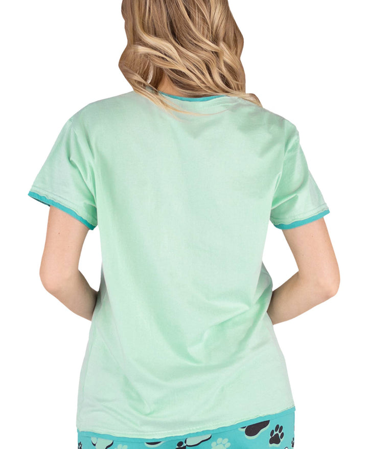 A person with wavy blonde hair is shown from the back in a light green Dog Mom, Cat Nap & More Pajama Tops cotton short-sleeve shirt and paw print patterned pants, set against a white background.
