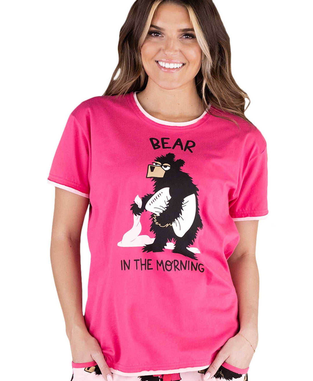 A smiling woman wears a Dog Mom, Cat Nap & More Pajama Top in soft pink cotton, featuring a cartoon bear with coffee and the playful text "Bear in the morning" above and below—a fun twist on novelty prints.