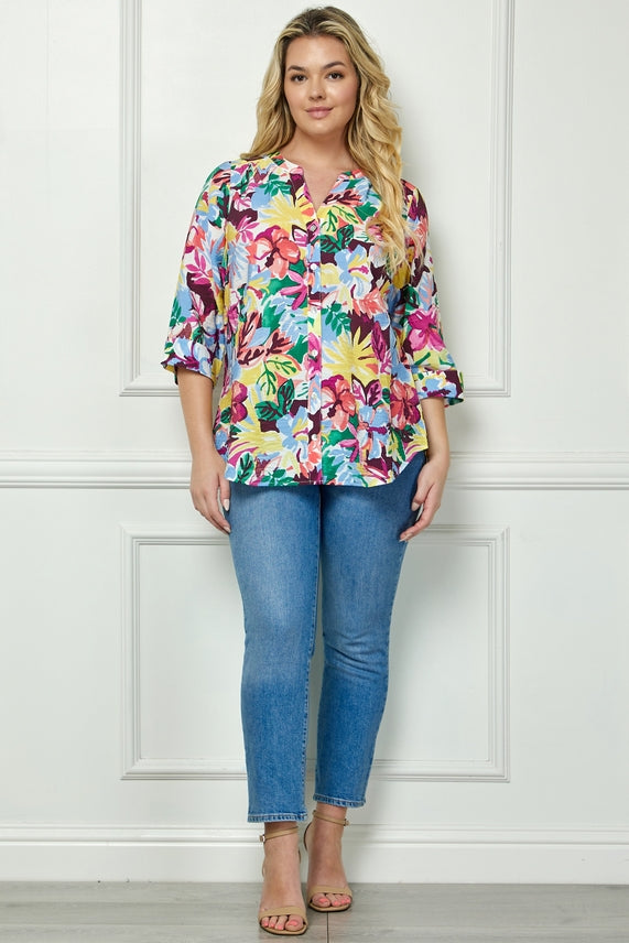 A woman with long blonde hair smiles slightly indoors against a white wall, wearing the Plus Floral Placket Blouse with three-quarter sleeves, light blue jeans, and beige open-toe heels.