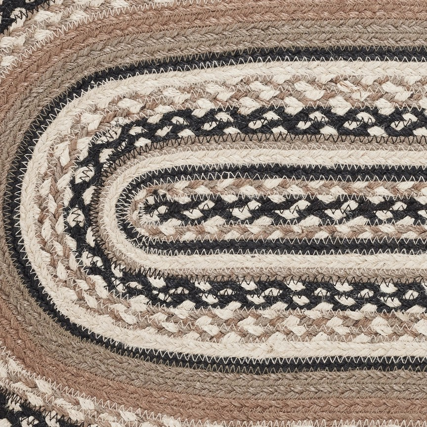 A close-up of a braided oval table runner with concentric bands of black, cream, tan, and brown woven texture.
