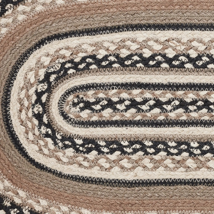 A close-up of a braided oval table runner with concentric bands of black, cream, tan, and brown woven texture.