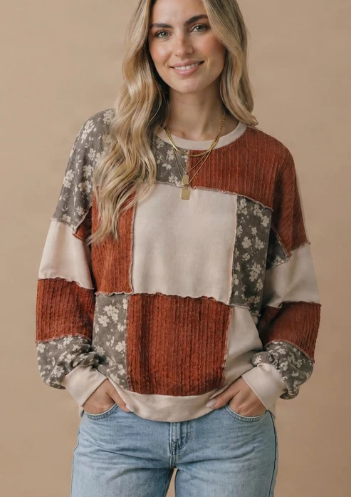 A woman with long, wavy blonde hair models the Color Block Knit Top—a relaxed fit women’s top with patchwork in rust, beige, and floral patterns—paired with light blue jeans. She stands against a beige background with her hands in her pockets.
