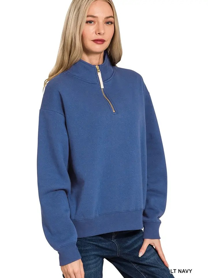A woman with long blonde hair wears the Fleece Half Zip Sweatshirt in a relaxed fit and light navy blue, paired with blue jeans, standing against a white background.