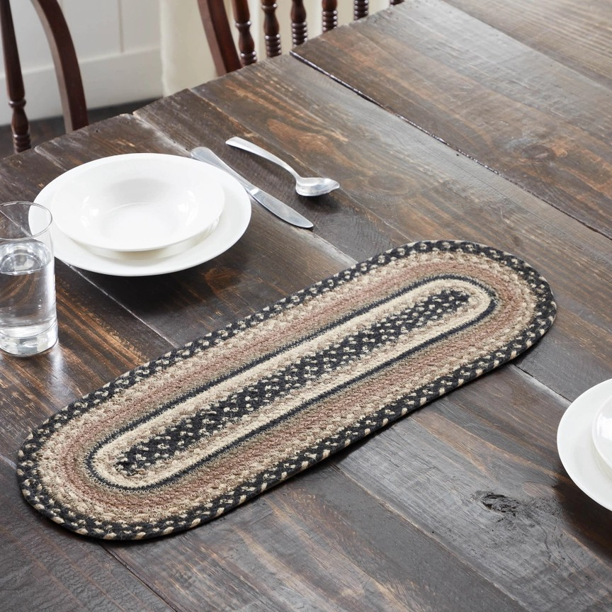 Oval braided table runner on a wooden table with white plates and silverware.