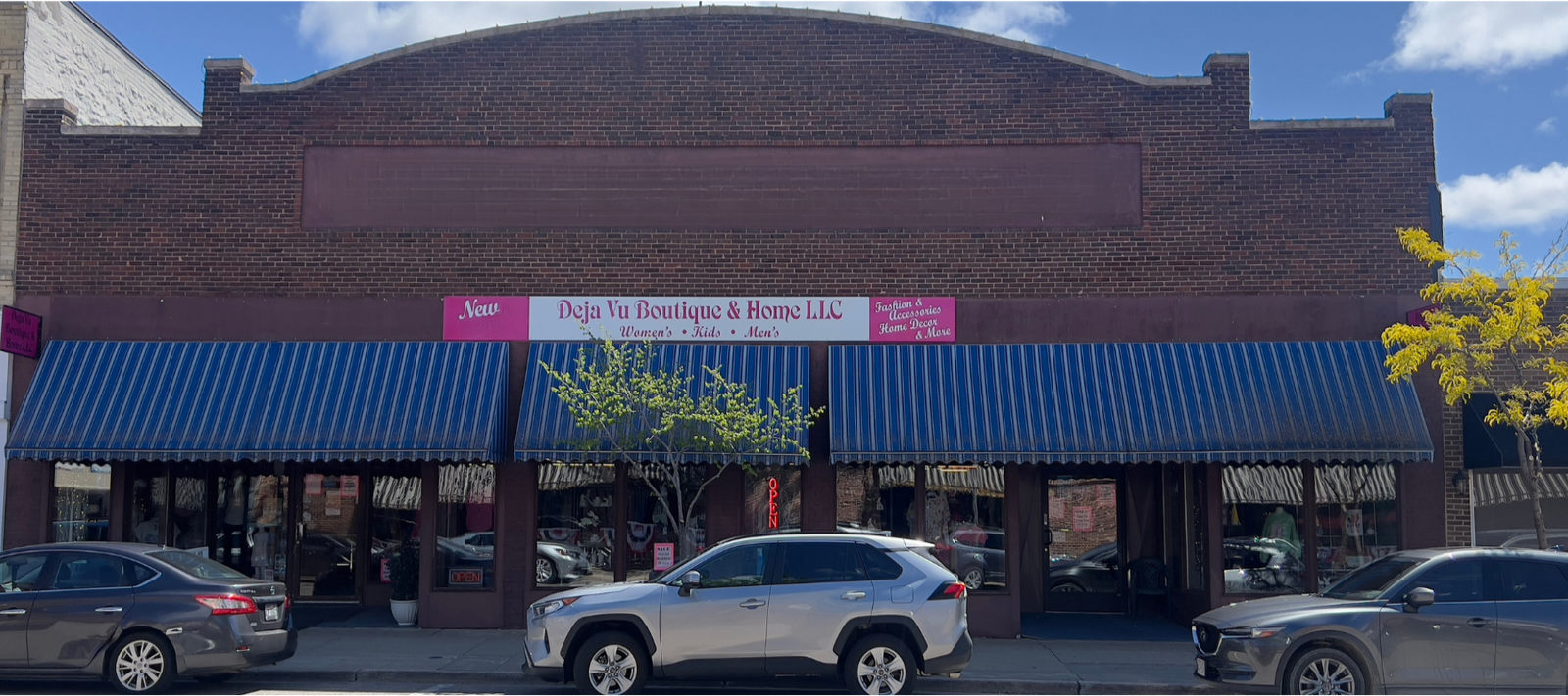 The image shows the storefront of Deja Vu Boutique & Home LLC in Ripon, WI. The building is a brick structure with a blue and white striped awning over the windows. There are cars parked in front of the building. The store's sign indicates they sell women's and kid's clothing.